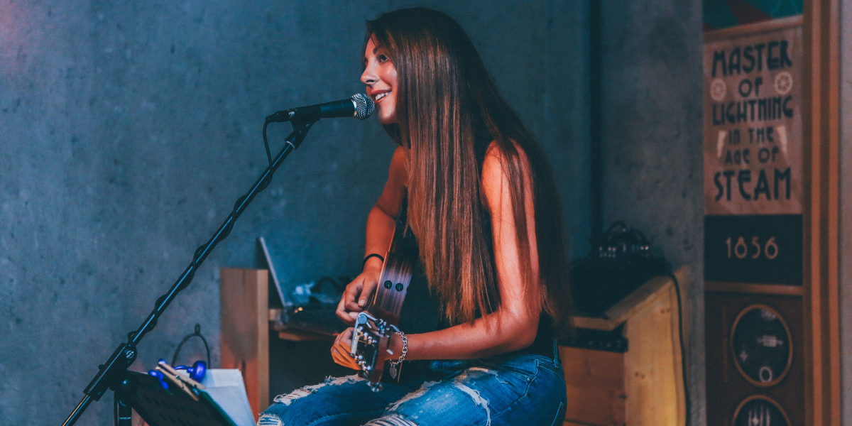 Young woman singing on a mic and play guitar sitting down