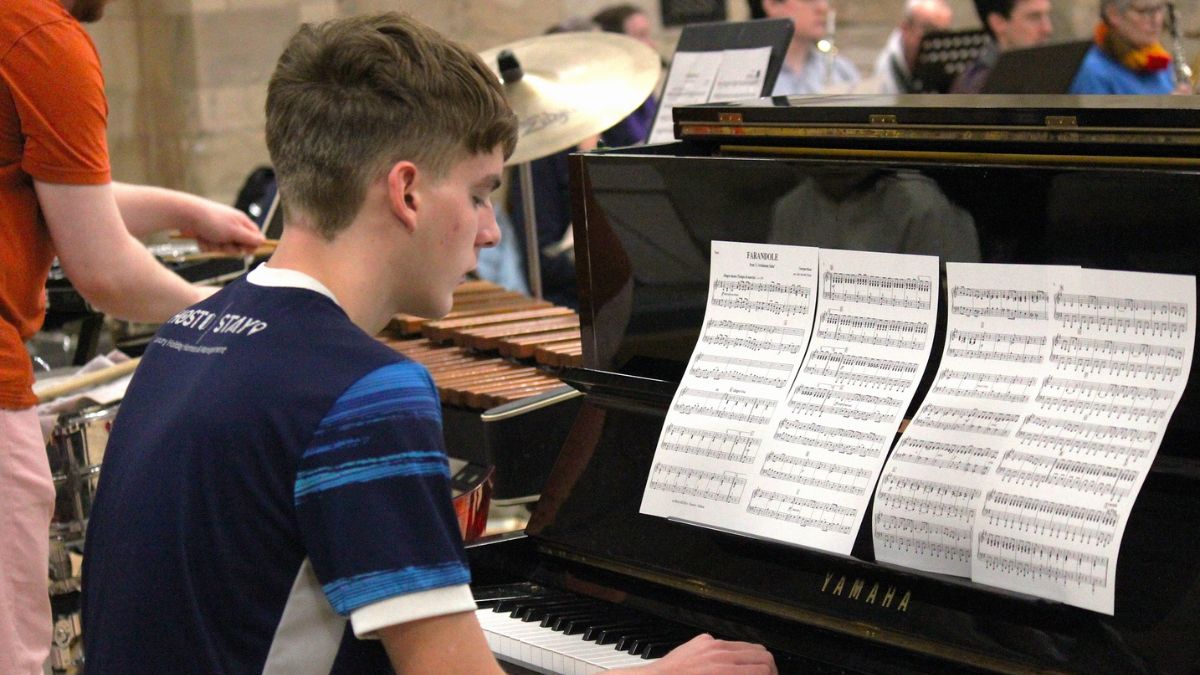 A young person playing an upright piano with sheet music