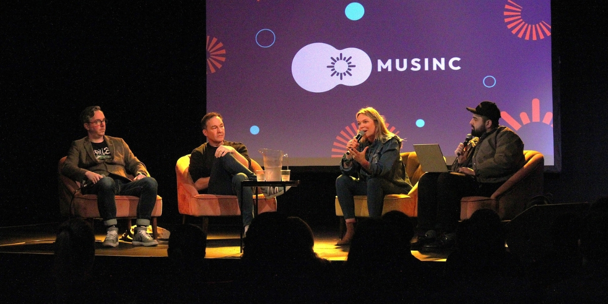 Four people with microphones sitting on sofas and conversing on a stage. The backdrop reads: Musinc.