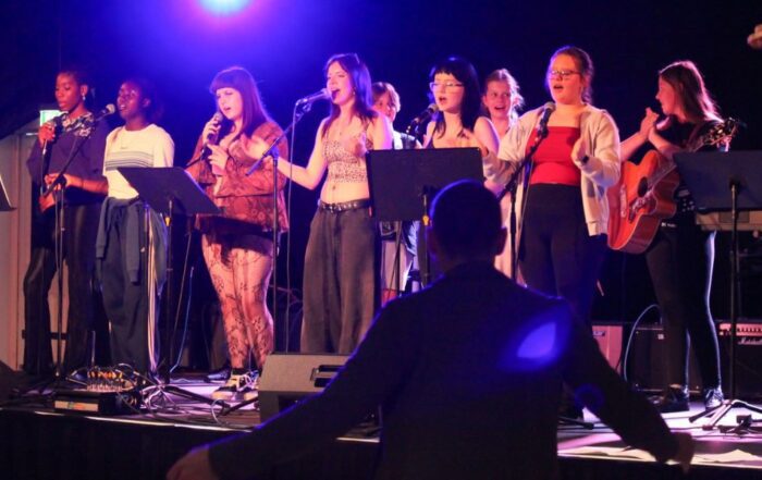 Young people singing on a stage in front of a facilitator