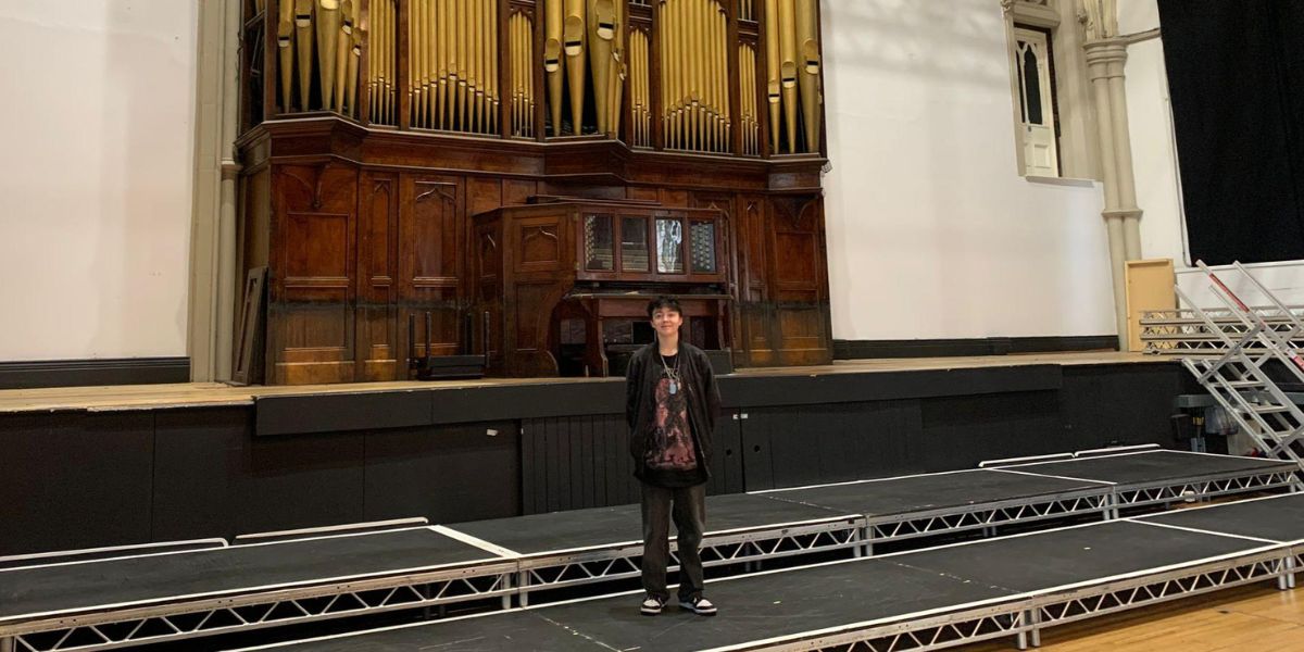 A young person standing on a stage in front of a pipe organ