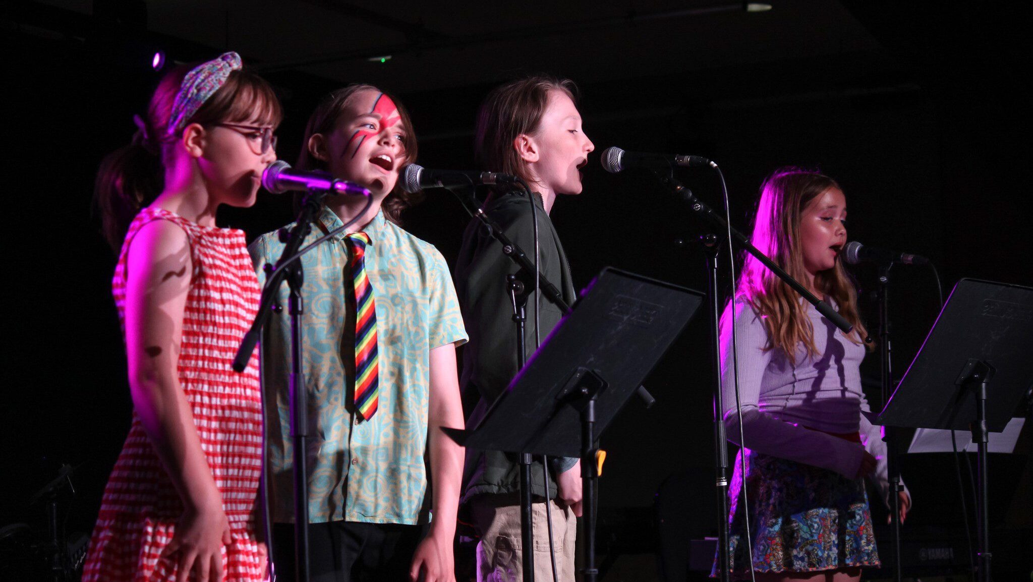 Four young people singing on a stage during a performance