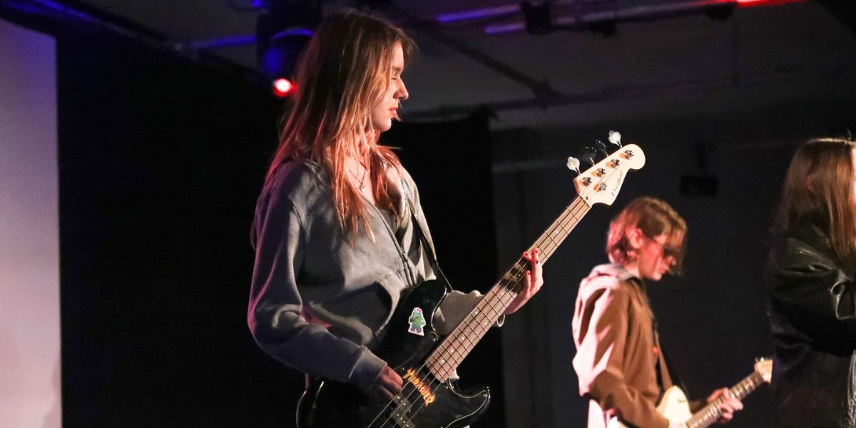 Two young people playing bass and electric guitar on a stage