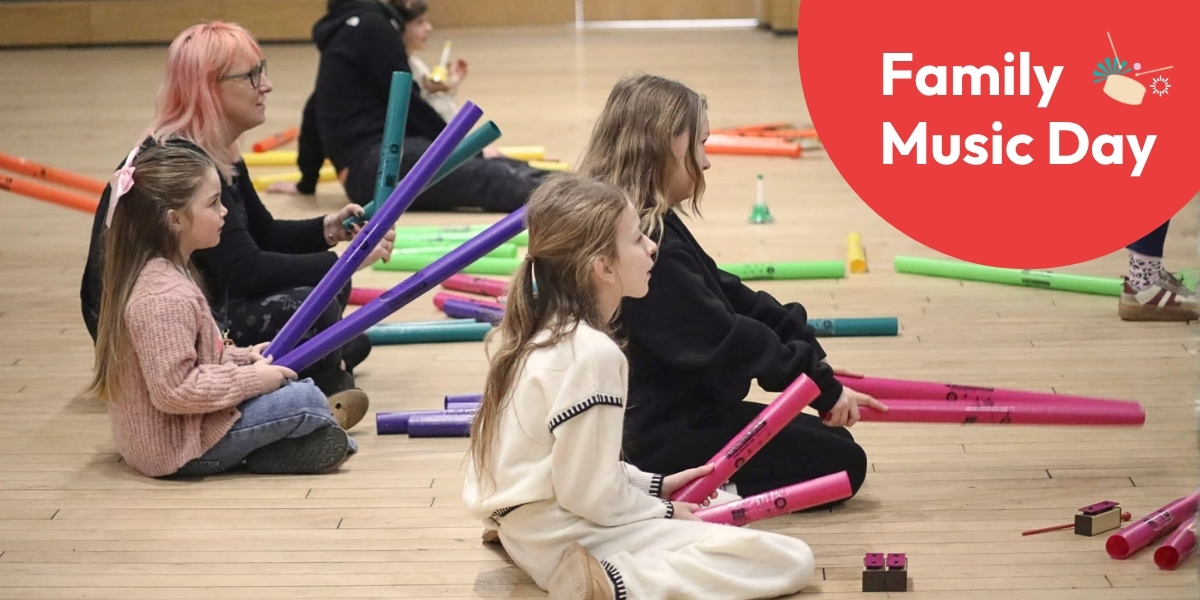 Children and their parents sitting on the floor playing Boomwhackers -colourful percussive tubes