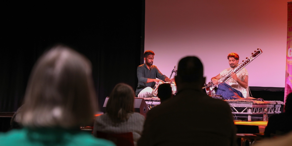 Musicians playing sitar and tabla on stage in front of an audience